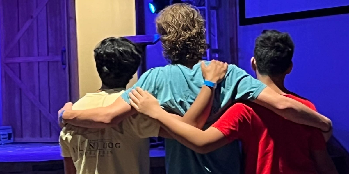 Three young men standing arm in arm during worship at a YMJA event
