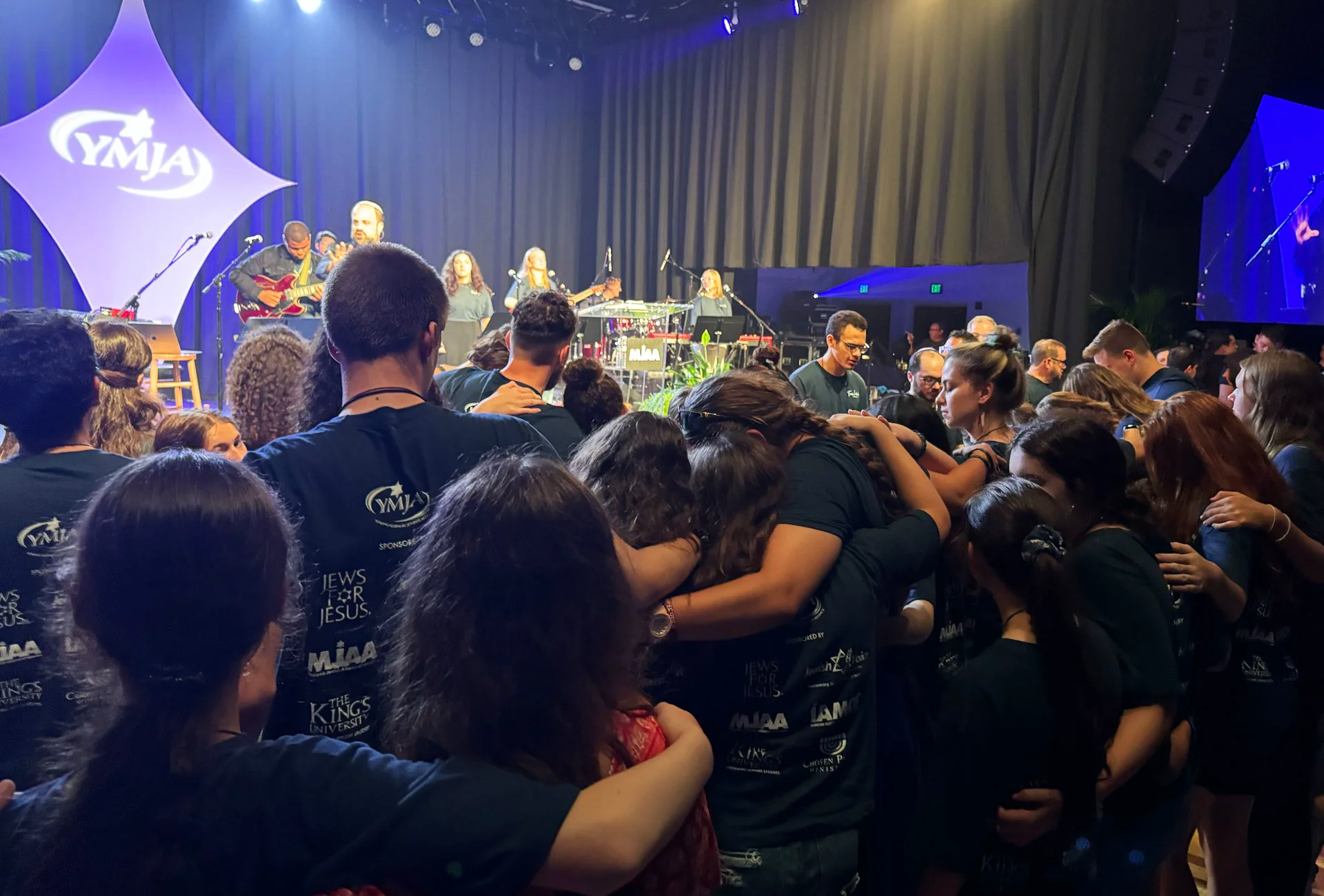 Young people in YMJA shirts worshipping together with arms around each other at a YMJA conference